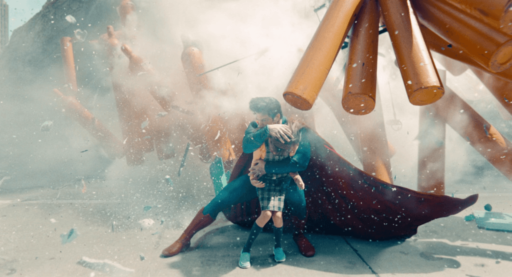 A screenshot from the 2025 Superman film of Superman protecting a small child.
