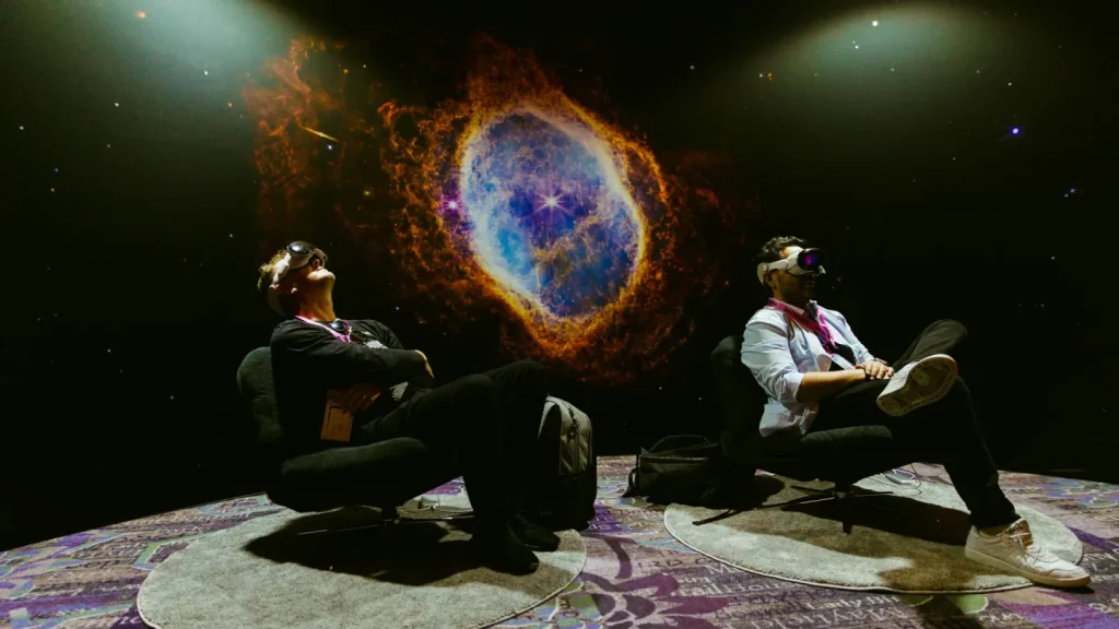 Two people sit on armchairs with VR experiences with an image of space behind them at SXSW 2025. 