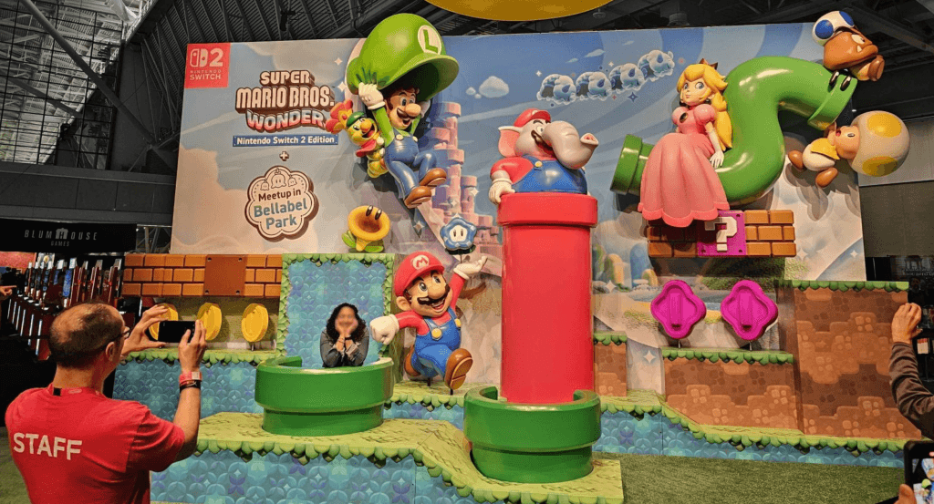 Screenshot of a woman being photographed by Nintendo staff in front of a giant Super Mario Bros. Wonder display