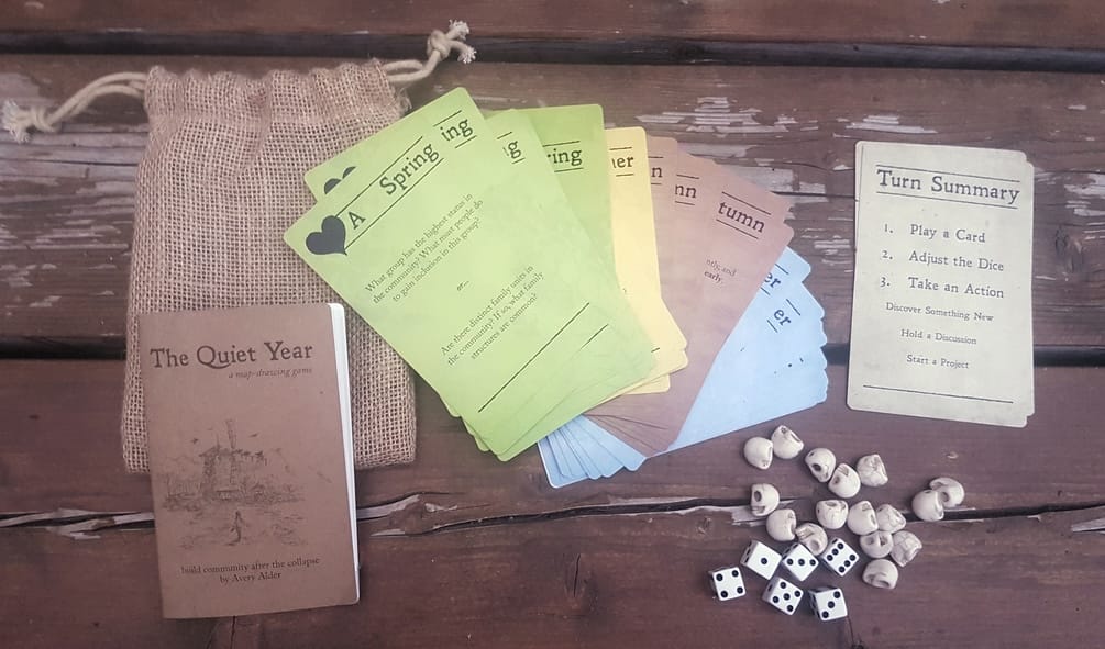 A bag set of the Quiet Year tabletop roleplaying game with a booklet, cards showing a spring, dice, skull icons, and a turn summary