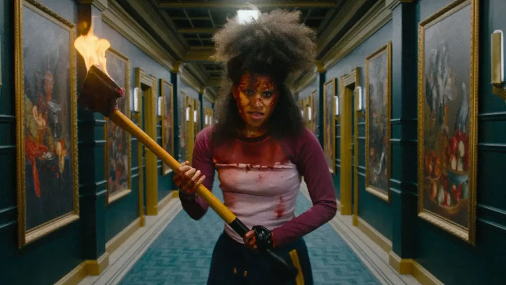 A screenshot from the upcoming 2026 film They Will Kill You, showing a woman walking down a long fancy hallway with an axe on fire. 