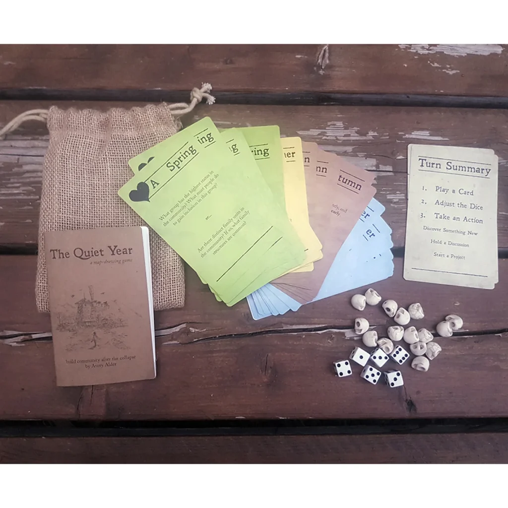 A photo of The Quiet Year, a TTRPG, and its bag kit that shows different cards and turn summary, featured in an Assemblage TTRPG review.