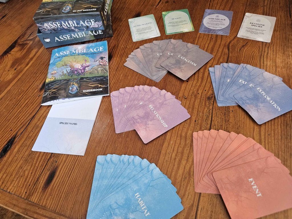 A photo of all the types of cards in the Assemblage TTRPG on a wooden table, featured in an Assemblage TTRPG review.