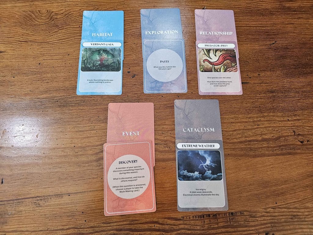 A close-up of cards available in the Assemblage TTRPG such as Verdant Gaia and Extreme Weather, featured in an Assemblage TTRPG review.
