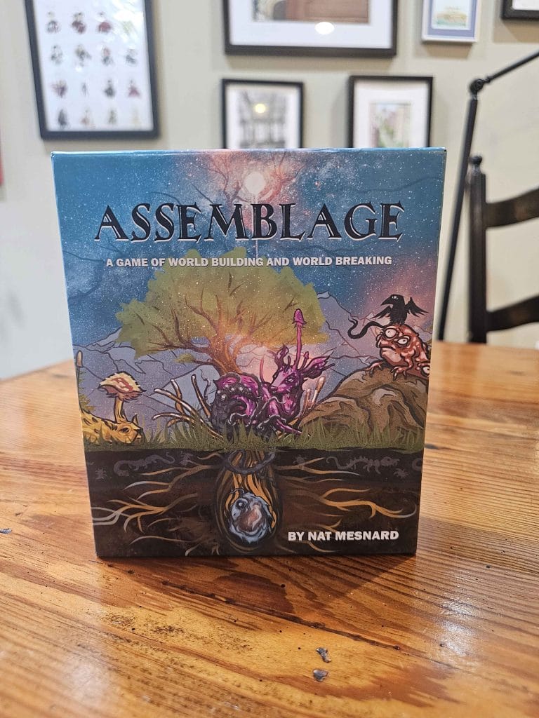 A photo of the box of Assemblage: A Game of World Building and World Breaking By Nat Mesnard on a wooden table, featured in a review of Assemblage