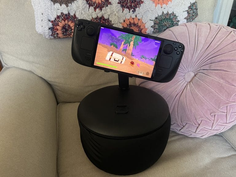 A photo of the Steam Deck on a Mechanism Gaming Pillow on an armchair and a pink pillow.
