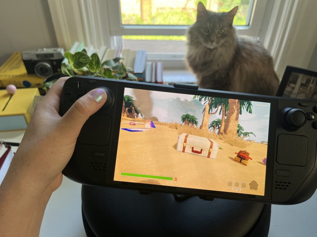 In a piece about the Steam Deck Mechanism Gaming Pillow, this photo shows a Steam Deck and a screenshot of the game PEAK with a cat looking on in the background.  