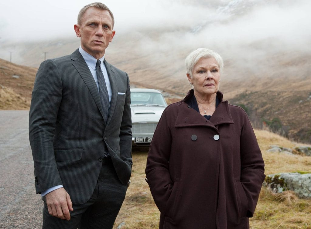 A screenshot from the 2012 James Bond movie Skyfall, showing Daniel Craig portraying James Bond next to Judi Dench portraying M. They wear suits and stand in a cold mountain valley in front of Bond's Aston Martin. This image is in an article about the character of Moneypenny in James Bond movies and video games.