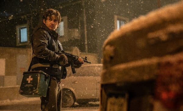Resident Evil (2026 film) - a man holding a submachine gun while looking backward in the snow, a green first-aid kit hanging over his shoulder, sitting at his waist