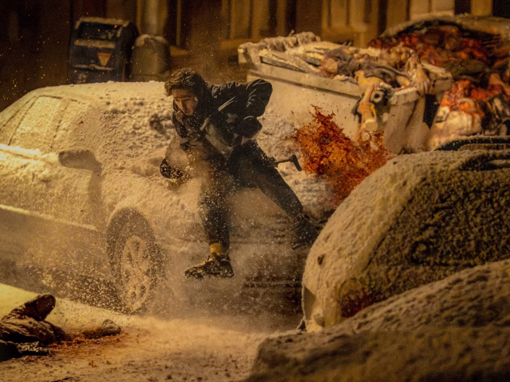 Resident Evil (2026 film) - Bryan running through snow-covered parked cars with bloodsplatter and a trail of dead bodies behind him
