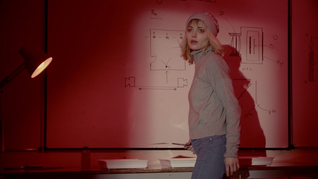 Tenebris Somnia Review: A screenshot of a blonde woman in a sweater walking in a red-lit room. 